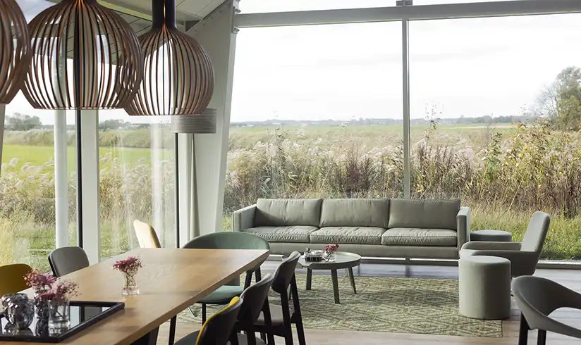 Grote ruimte met tafels en stoelen en grote ramen met uitzicht op weilanden